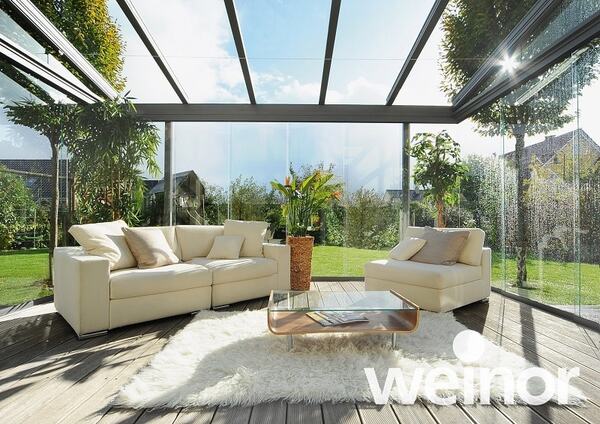 Modernes Wohnzimmer im Wintergarten mit Glasdach, gemütlichen Sofas und Gartenblick.